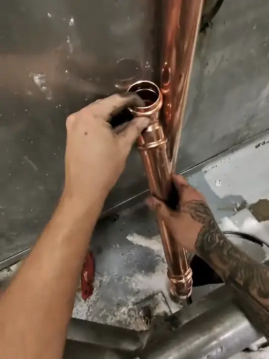 Through Jacob's glasses: hands fitting a copper riser beside stainless equipment