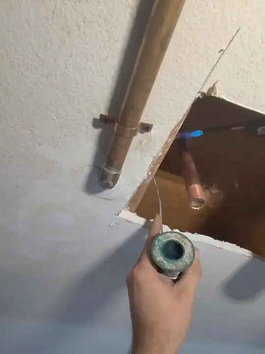 Solder At A Stub-Out: A copper stub through an opening in a wall, solder in hand, before the wall is closed up.