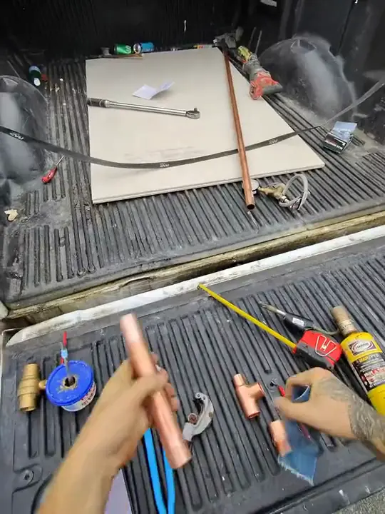 Through Jacob's glasses: copper fittings, a ball valve and tools laid out on a truck tailgate